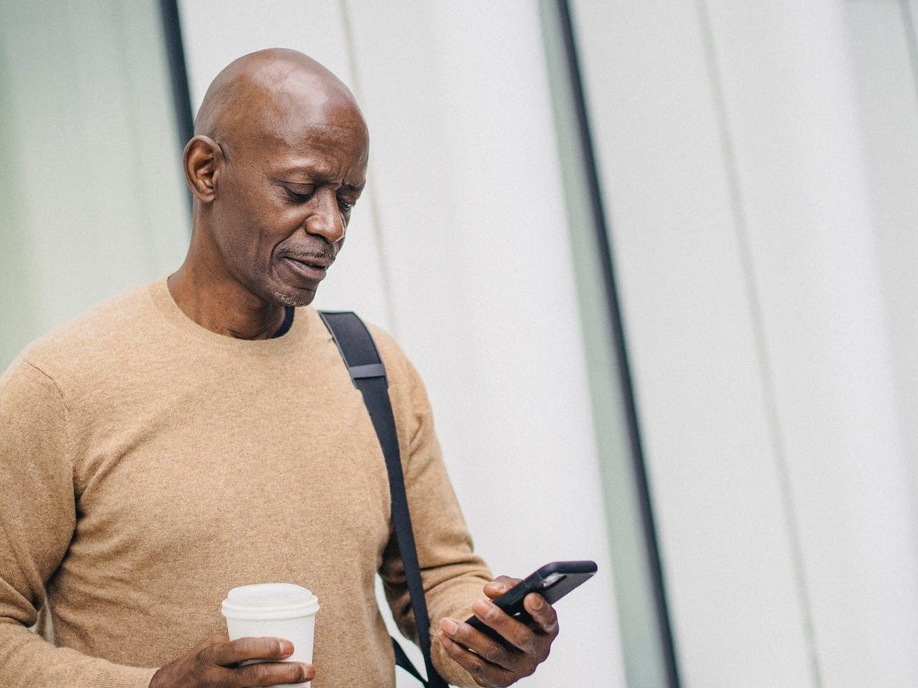 serious black man with smartphone and takeaway coffee